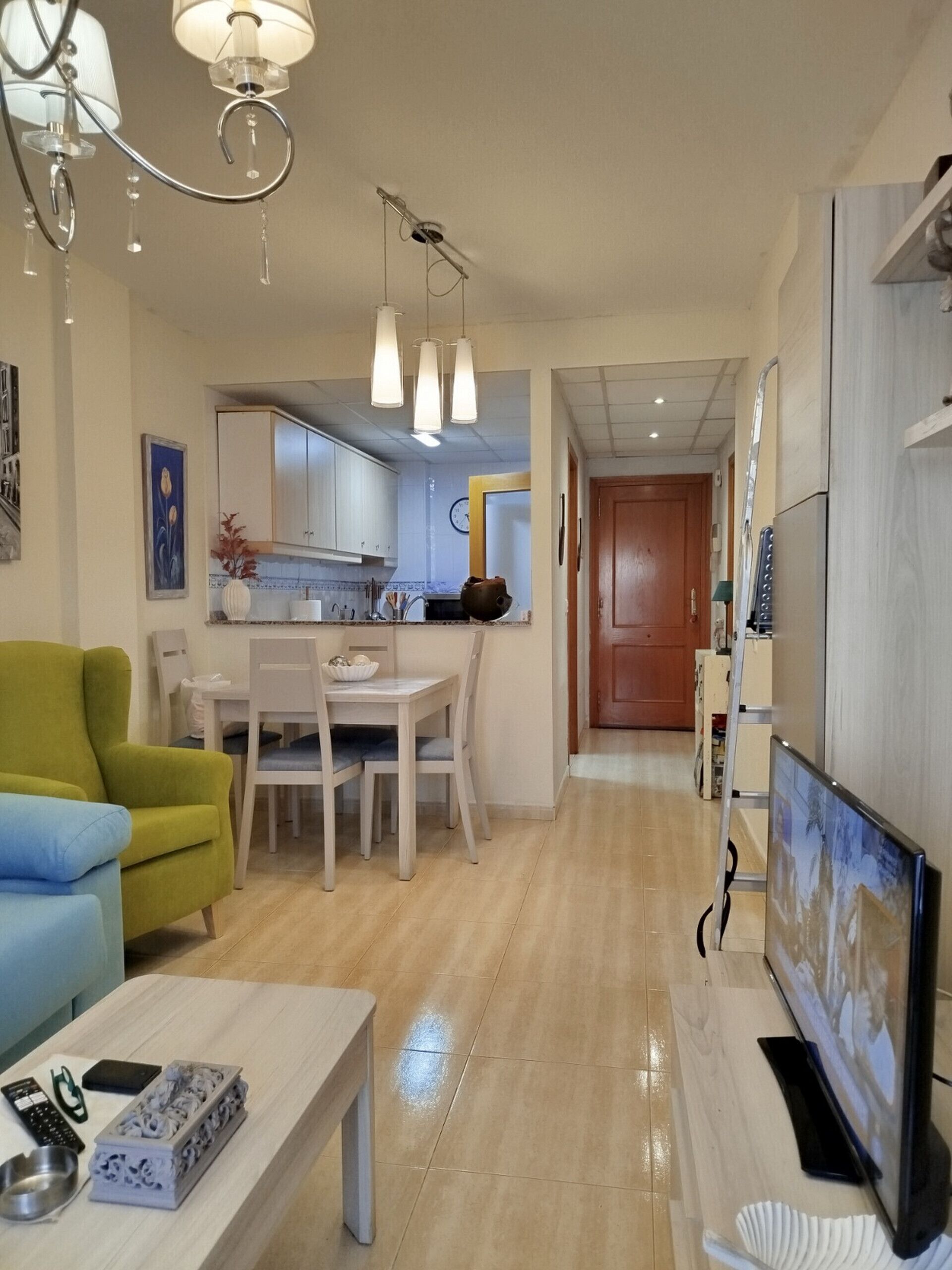 Uma sala de estar moderna com televisão, uma área de jantar com mesa e cadeiras, e uma cozinha ao fundo.