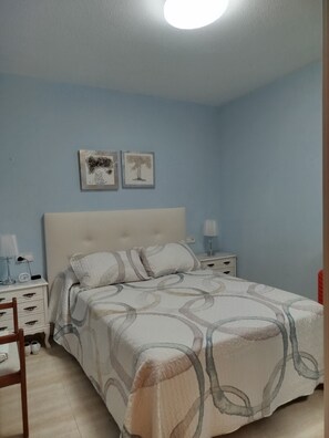 Ein Schlafzimmer mit Bett, Nachttischen, einem Sessel und Wandbildern.