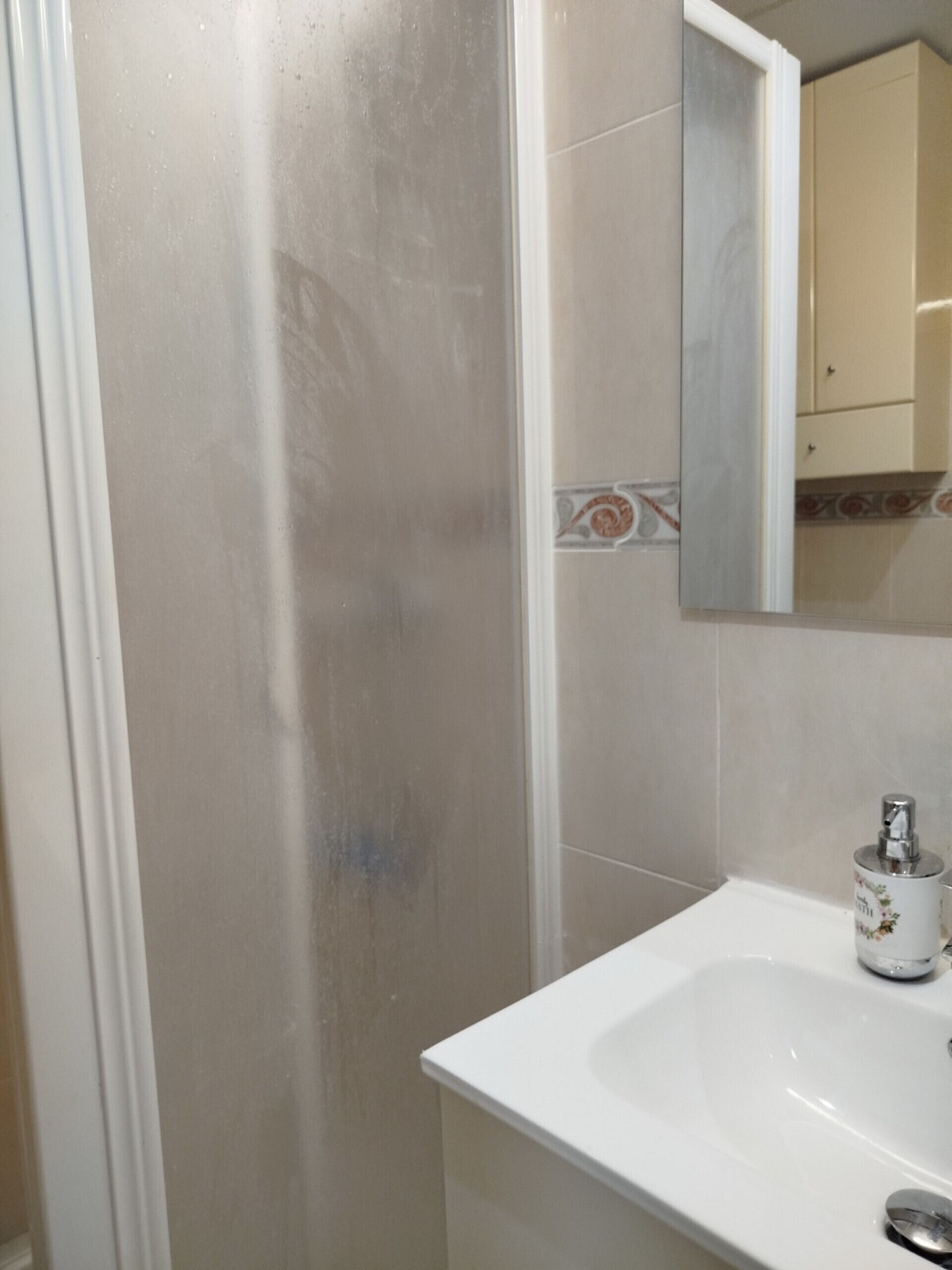 Casa de banho com lavatório branco, espelho e zona de duche.