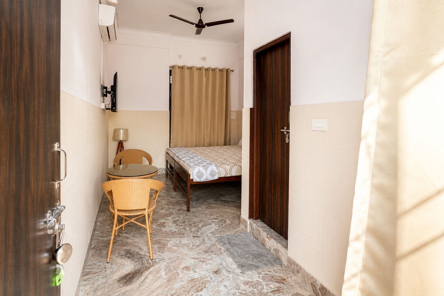A narrow hallway leading to a bedroom with a bed, a chair, a table, and a ceiling fan.