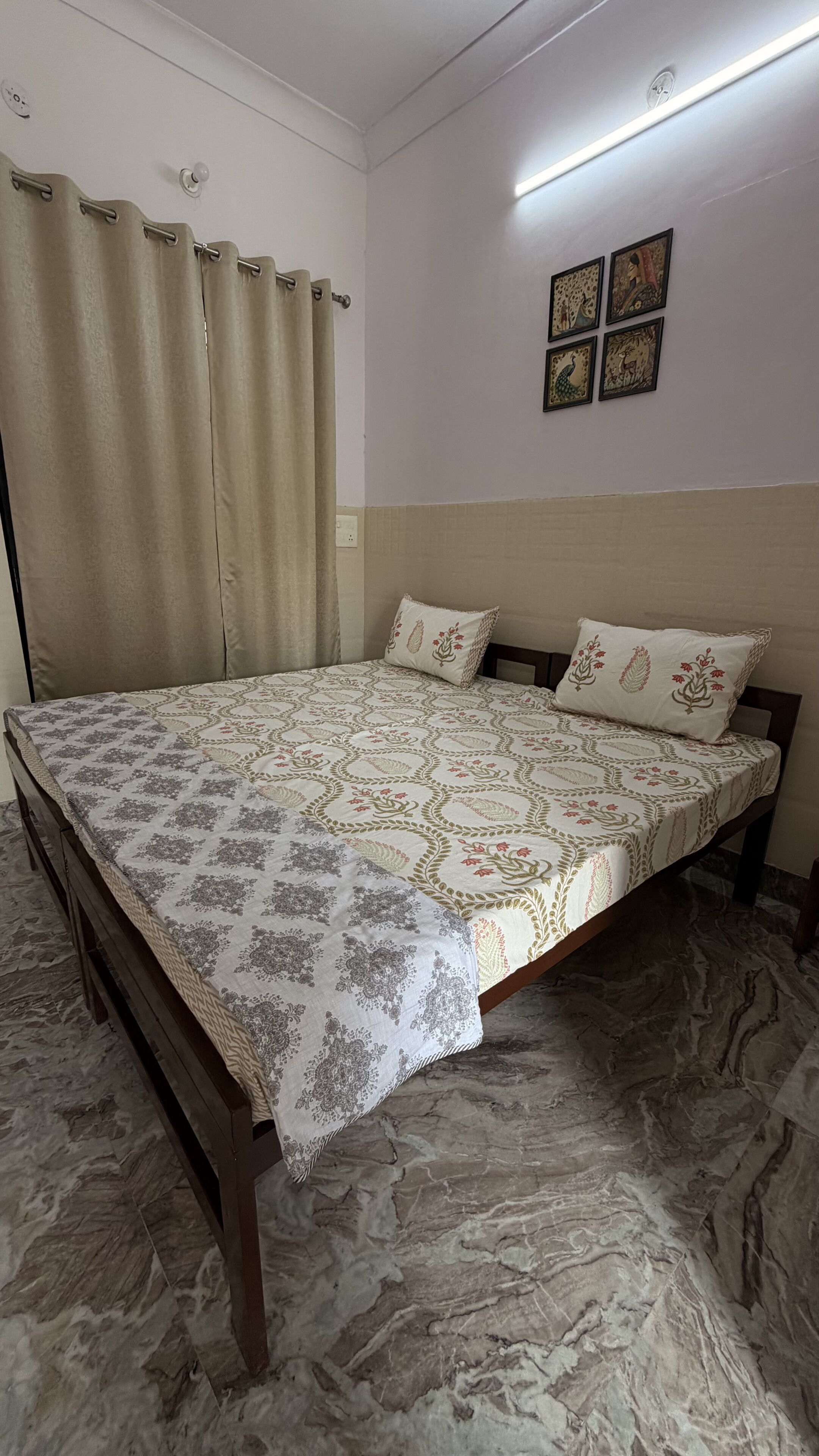 A bedroom with a bed, curtains, a wall with artwork, and a marble floor.