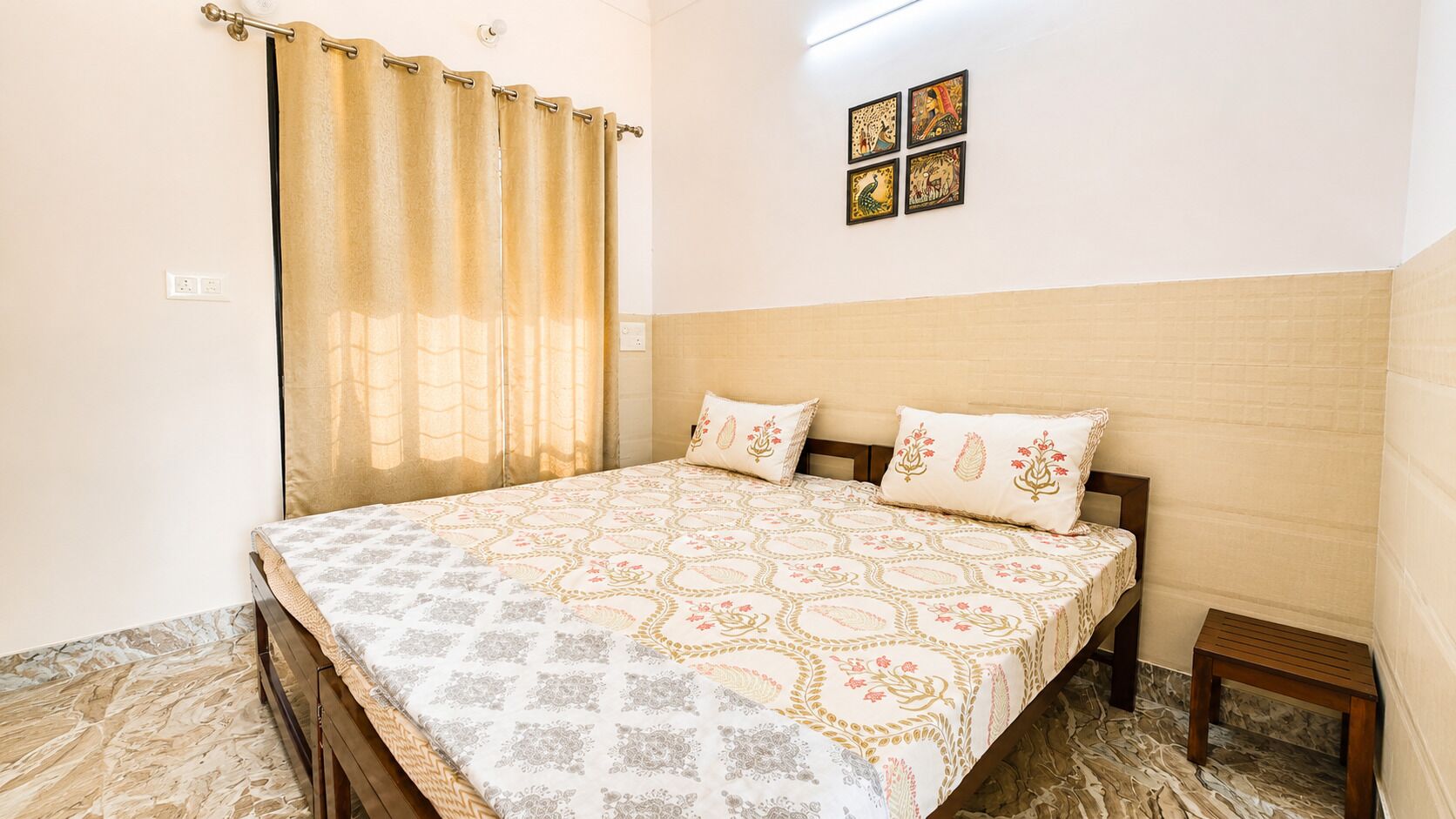A bedroom with a bed, curtains, a wall-mounted artwork, and a small wooden stool.