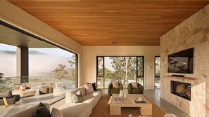 A modern living room with a stone fireplace, large windows, and a view of a natural landscape. - The Lakehouse, Kangaroo Valley (Kangaroo Valley)