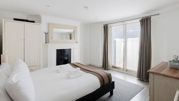 A hotel room with a bed, a fireplace, a wardrobe, a mirror, and a view of the outdoors. - Lovely Garden Flat in Kentish Town (Greater London)