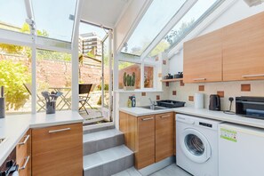 Une cuisine moderne avec des meubles en bois, un lave-linge encastré et une vue sur le jardin grâce à de grandes fenêtres.