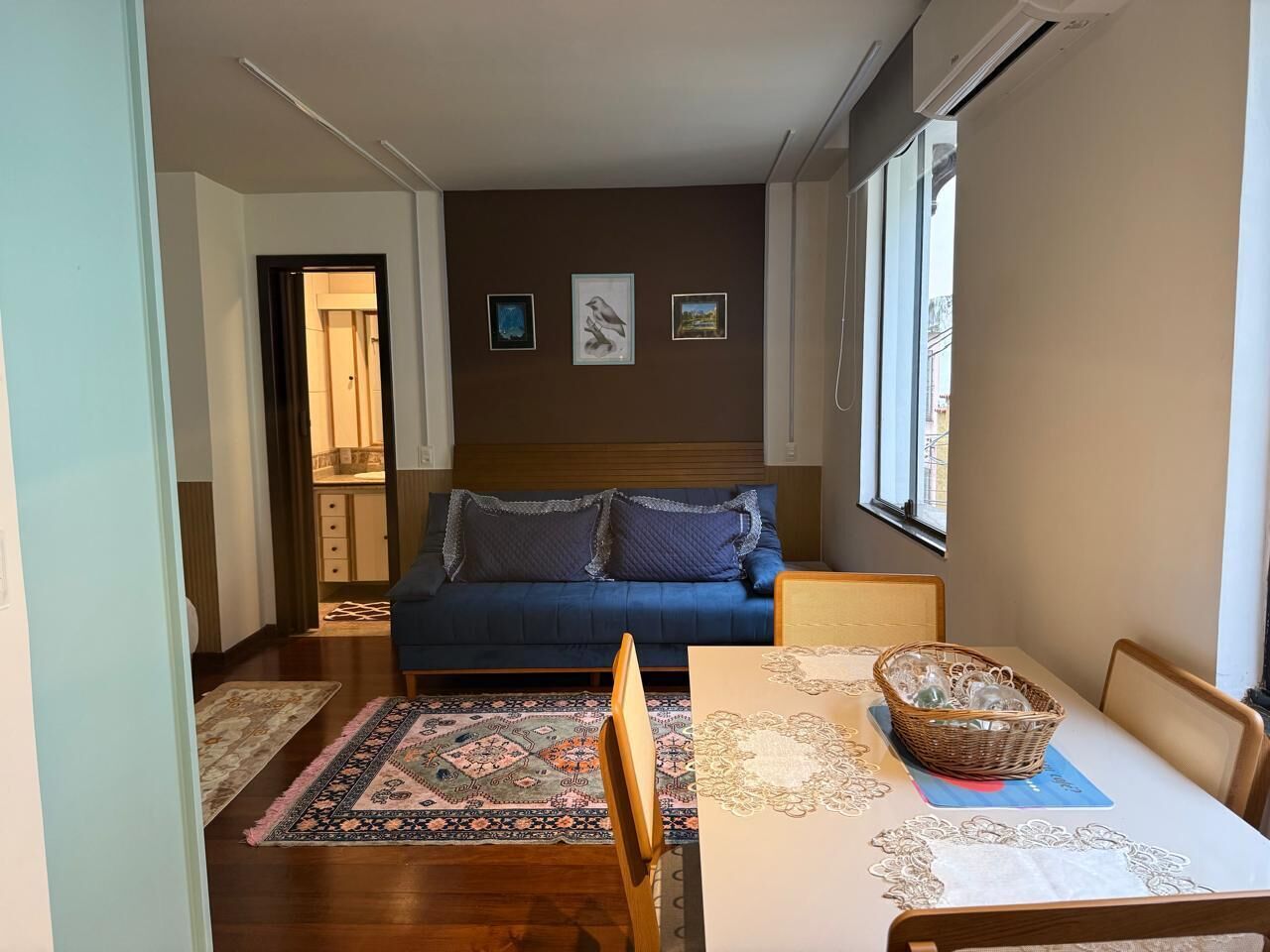 Una sala de estar con un sofá, una mesa de comedor con sillas, un tapete estampado y una pared decorada con cuadros.