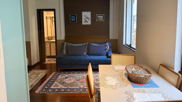 A living room with a sofa, a dining table with chairs, a patterned rug, and a wall with framed pictures. - Vista Villa Premium Apartment | Copacabana (Rio de Janeiro)