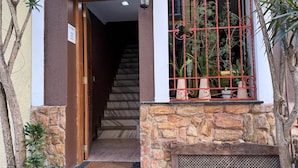 A building entrance with a stone facade, a wooden door, a staircase, and a window with a red metal grille. - Vista Villa Premium Apartment | Copacabana (Rio de Janeiro)