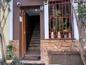 A building entrance with a stone facade, a wooden door, a staircase, and a window with a red metal grille. - Vista Villa Premium Apartment | Copacabana (Rio de Janeiro)