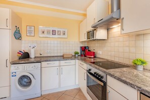 A modern kitchen with a built-in washing machine, a microwave, and a gas stove. - Family-friendly vacation rental with a garden and a fireplace (Karlshagen)