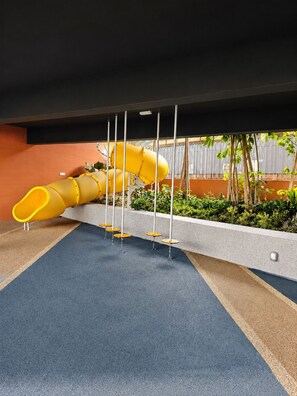 Ein Spielplatz mit einer gelben Rutsche und einem blauen, gummiartigen Boden.