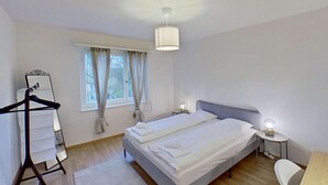 A bedroom with a bed, a bedside table, a lamp, a hanging light fixture, a window with curtains, and a wardrobe. - Charming 3 Bedroom Retreat (Zürich)