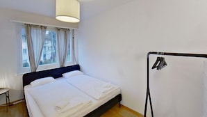 A bedroom with a bed, a window with curtains, a hanging clothes rack, and a lamp. - Charming 3 Bedroom Retreat (Zürich)