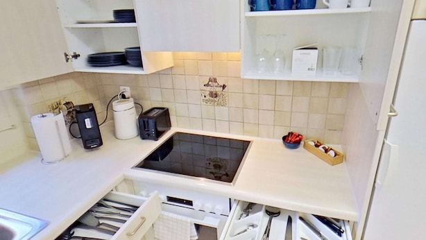 A compact kitchen with a microwave, toaster, and coffee maker on the countertop, a small sink, and a cabinet with dishes. - Charming 3 Bedroom Retreat (Zürich)
