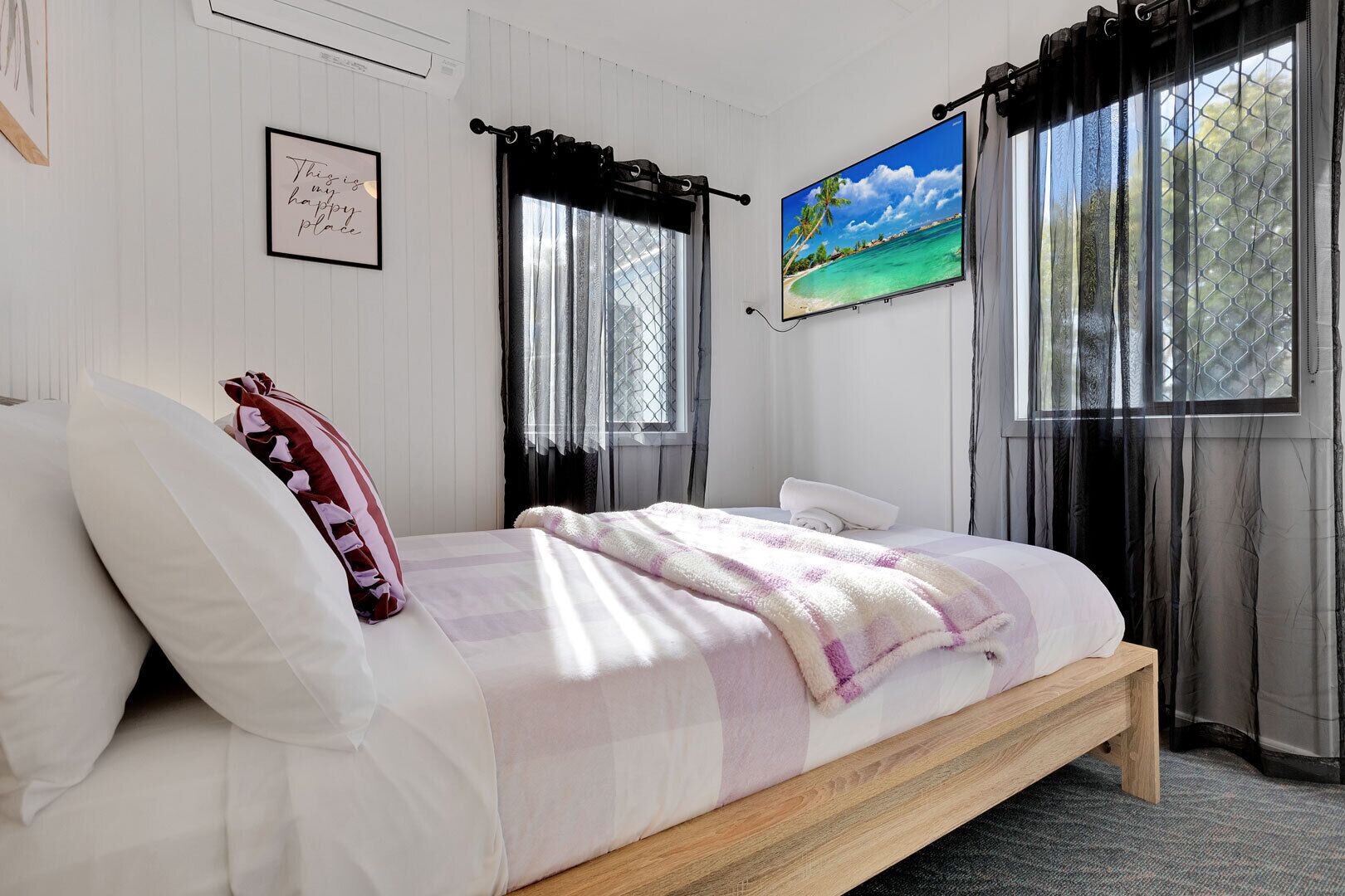 A bedroom with a bed, a framed quote on the wall, a painting, and a window with curtains.
