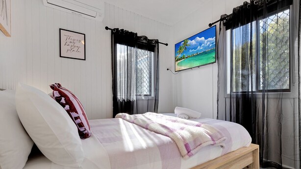 A bedroom with a bed, a framed quote on the wall, a painting, and a window with curtains. - Lyrebird Hideaway: Pet Friendly, Peaceful & Private Retreat (Lakes Entrance)