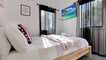 A bedroom with a bed, a framed quote on the wall, a painting, and a window with curtains.