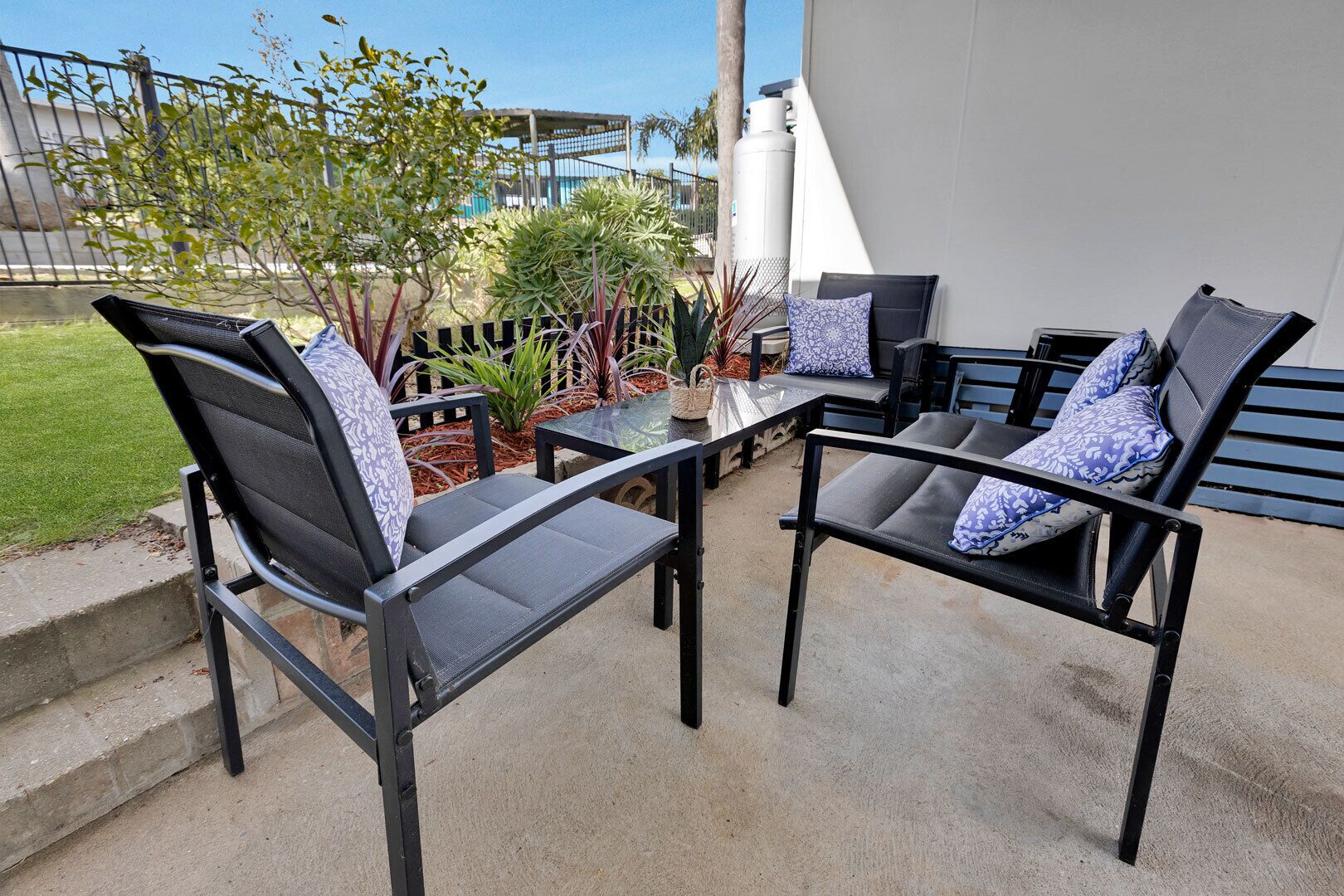 An outdoor seating area with two chairs and a table, surrounded by plants and a view of a building.
