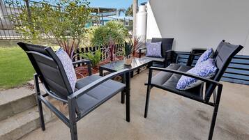 An outdoor seating area with two chairs and a table, surrounded by plants and a view of a building.