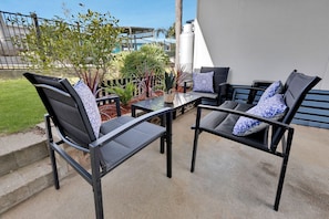 An outdoor seating area with two chairs and a table, surrounded by plants and a view of a building.