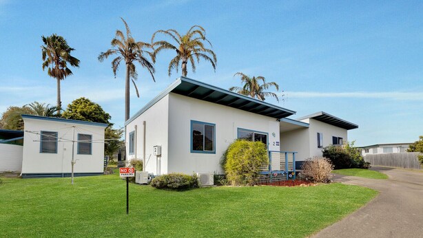 A single-story mobile home with a white exterior and blue trim, a front porch, and a small attached garage. - Lyrebird Hideaway: Pet Friendly, Peaceful & Private Retreat (Lakes Entrance)