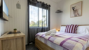 A bedroom with a bed, a bedside table, a window with curtains, a wall-mounted TV, and a framed picture. - Lyrebird Hideaway: Pet Friendly, Peaceful & Private Retreat (Lakes Entrance)