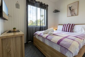 A bedroom with a bed, a bedside table, a window with curtains, a wall-mounted TV, and a framed picture.