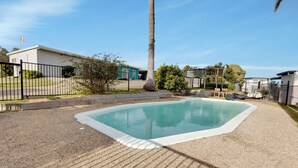A rectangular swimming pool with a surrounding gravel area and a palm tree. - Lyrebird Hideaway: Pet Friendly, Peaceful & Private Retreat (Lakes Entrance)