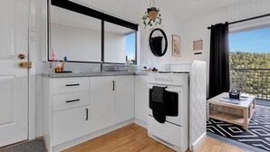 A modern kitchen with white cabinets, a built-in oven, and a small dining area with a table and chairs. - Lyrebird Hideaway: Pet Friendly, Peaceful & Private Retreat (Lakes Entrance)