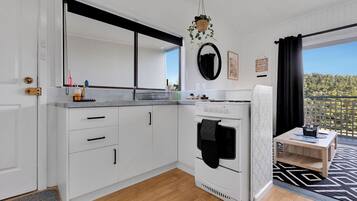 A modern kitchen with white cabinets, a built-in oven, and a small dining area with a table and chairs.