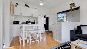 A modern kitchen with white cabinets, a microwave, and a small dining area with stools. - Lyrebird Hideaway: Pet Friendly, Peaceful & Private Retreat (Lakes Entrance)