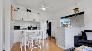 A modern kitchen with white cabinets, a microwave, and a small dining area with stools.