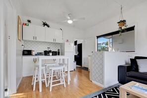 A modern kitchen with white cabinets, a microwave, and a small dining area with stools.