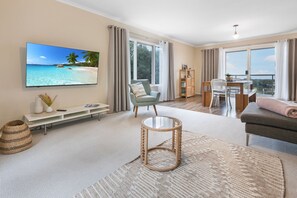 A living room with a flat-screen TV, a sofa, a round coffee table, and a dining area with a table and chairs. - The views at Eastern Views Beach House alone are worth the stay! (Lakes Entrance)