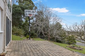 Ein Basketballplatz mit Korb, umgeben von einem gepflasterten Weg und Bäumen.