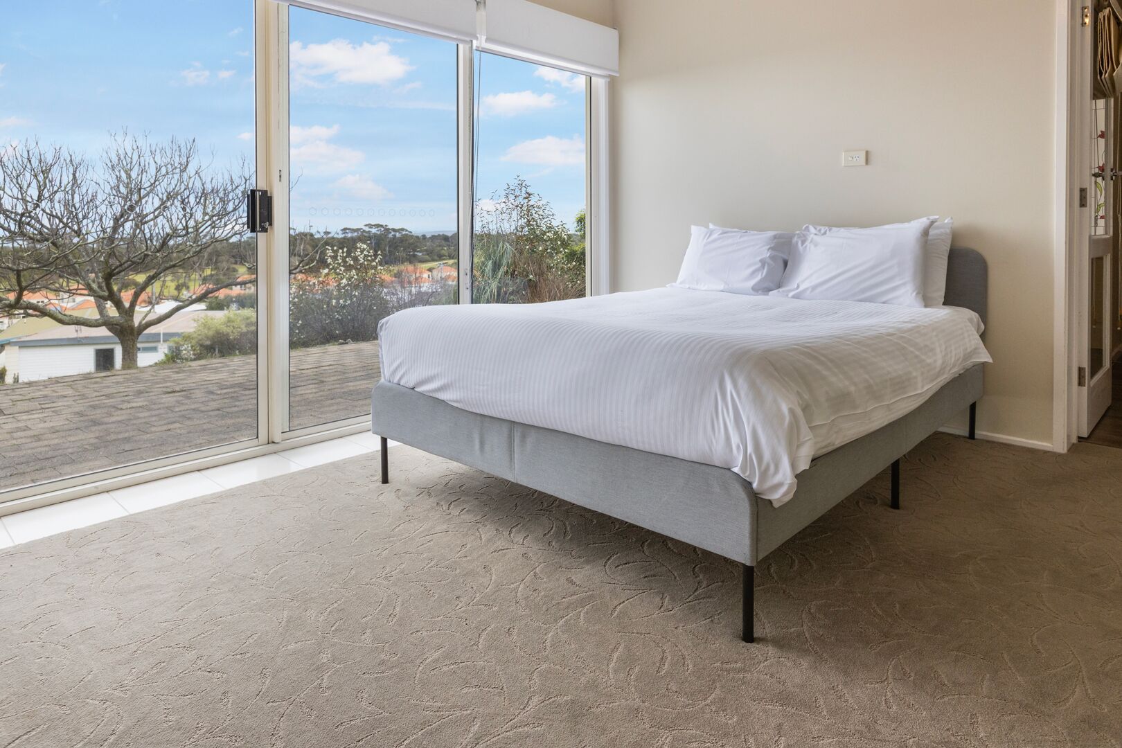A bedroom with a bed, a large window, and a view of the outside.