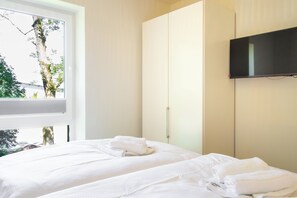 A hotel room with a bed, a television mounted on the wall, and a window with a view of trees and a building. - Tide Resort 2a DG - Sauna. Balcony. Meernah. (Tossens)