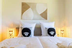 A hotel room with a large bed, two pillows with a sheep design, a wall art piece, and two bedside lamps. - Tide Resort 2a DG - Sauna. Balcony. Meernah. (Tossens)