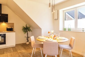A modern kitchen with a dining area, featuring a round table with chairs, a potted plant, and a window with a view of a building. - Tide Resort 2a DG - Sauna. Balcony. Meernah. (Tossens)
