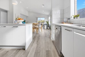 A modern kitchen with white cabinetry, a central island, and a dining area with wooden chairs. - Coast and Canopy is the perfect place to slow down and reconnect (Eagle Point)