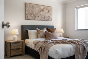 Ein Schlafzimmer mit einem Bett, zwei Nachttischen, einem Wandbild und einem Fenster.