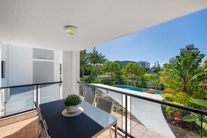 Un balcón con mesa y sillas, con vista a una piscina y follaje.