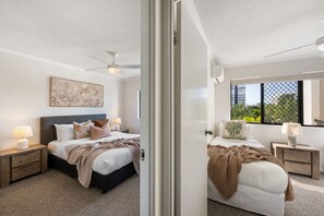 Un dormitorio moderno con cama, mesitas de noche, ventilador de techo y ventana con vistas.
