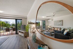 A modern living room with a large mirror, a sofa set, a TV, and a dining area with chairs and a table. - 2BR Pool-view apartment at Mirage Resort (Alexandra Headland)