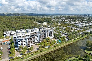 A residential area with modern apartment buildings, a river, and a park with a walking path. - 2BR Pool-view apartment at Mirage Resort (Alexandra Headland)