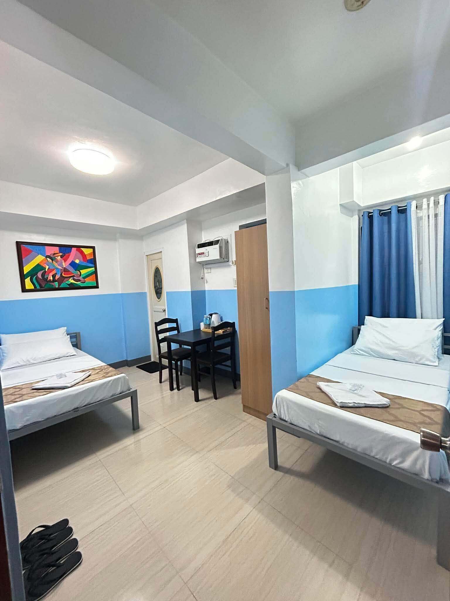 A hotel room with two beds, a dining table, chairs, a painting, and a door.