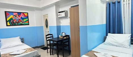 Une chambre d’hôtel avec deux lits, une table à manger, des chaises, un tableau et une porte.