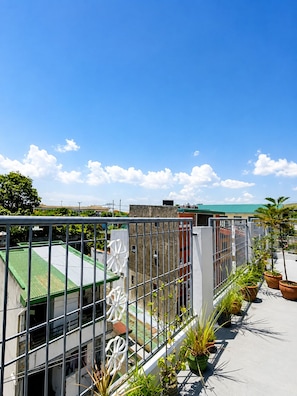A rooftop with a metal railing, potted plants, and buildings in the background. - Metrohive Apartment 3B - Cozy Studio Near Airport & PITX (Pasay City)
