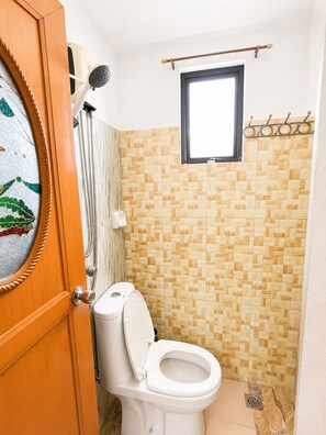 A bathroom with a toilet, a shower with a handheld showerhead, and a window. - Metrohive Apartment 3B - Cozy Studio Near Airport & PITX (Pasay City)