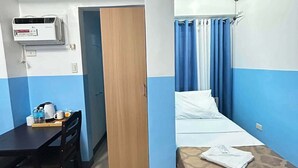 Una camera d'albergo con un letto, una scrivania, una sedia, un armadio e un condizionatore.